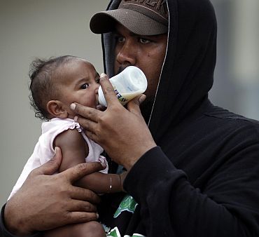 A local resident feeds his baby outside an emergency cyclone shelter after it was declared full and the gate locked