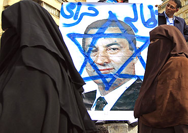 Women walk past an opposition supporter holding a poster of Egyptian President Hosni Mubarak