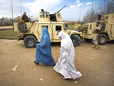 Afghan women walk past a US military vehicle of NATO's International Security Assistance Force in Siavashan village near Herat