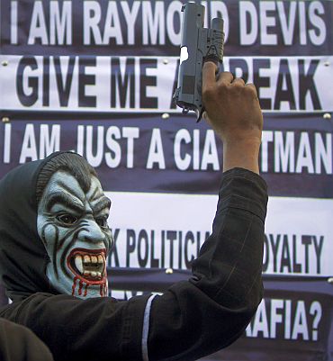 A supporter of a political party poses with a mask and toy gun during a protest against Raymond Davis