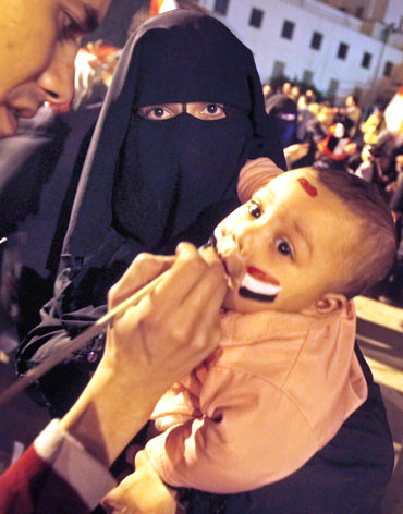 An opposition supporter holds her child as an Egyptian flag is painted on her baby's face