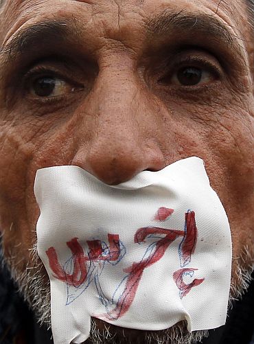 An anti-government demonstrator looks on with a sign reading 'shut up' over his mouth