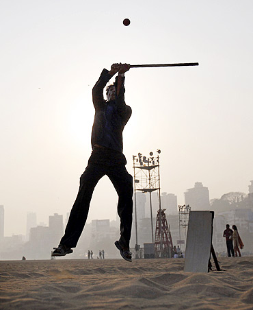 A man hits a ball by the beach with a stick for a bat and a piece of wood for wickets in Mumbai.