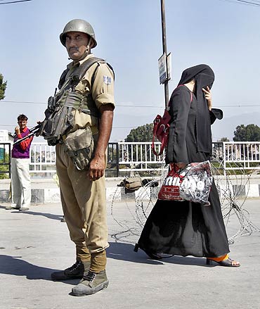 A Kashmiri woman walks past a policeman standing guard at a barricade during a curfew in Srinagar