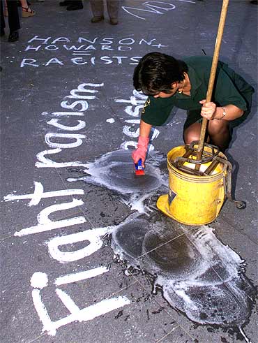 An ethnic Chinese cleaner scrubs off anti-racist slogans scribbled on the street by protesting students in Sydney
