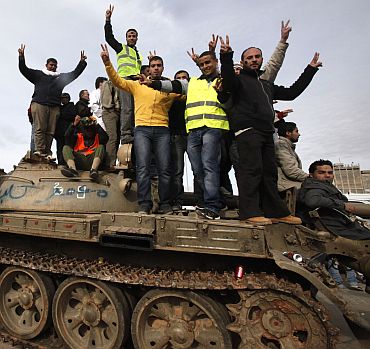Anti-government protesters make victory signs as they stand on an army tank
