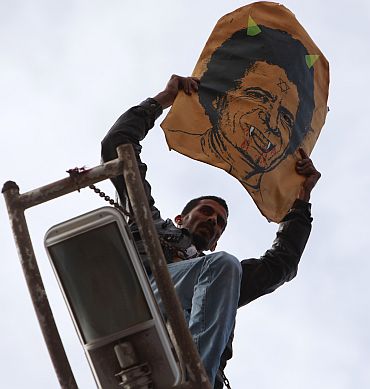 A protester holds a poster depicting Libyan leader Muammar Gaddafi as he stands over a lamp post in Benghazi city
