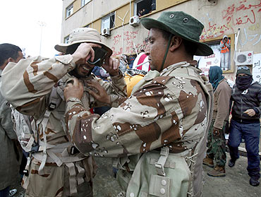 Anti-government demonstrators help each other wear army uniforms which they took over after troops loyal to Libyan leader Muammar Gaddafi fled the city following clashes in Benghazi