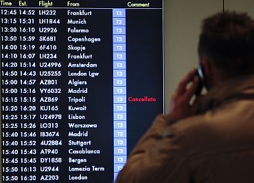 A man talks on the mobile phone as he watches the flight board showing a cancelled flight from Tripoli at the Leonardo Da Vinci International airport in Rome