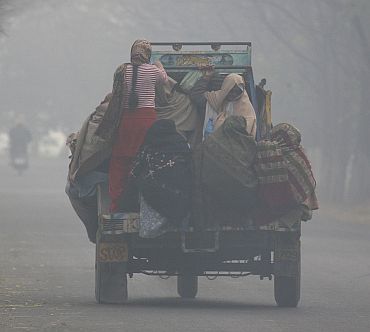 Women travel on the back of a vehicle on a cold and foggy day near Chhuni village in Punjab
