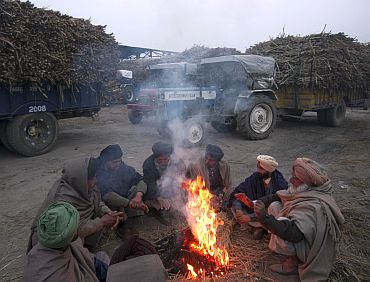 Farmers warm themselves by a fire as they wait to sell their sugarcane crop at a mill on a cold morning at Morinda in Punjab