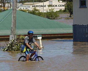 A man rides his bicycle on a street affected by flood waters in Bundaberg, Queensland