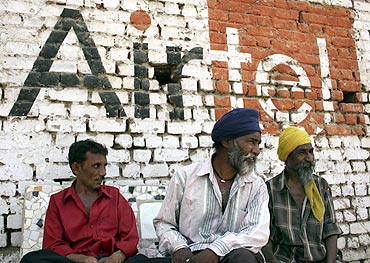 Men sit in front of a wall advertising Bharti Airtel at a roadside in Ahmedabad