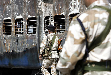 Rapid Action Force personnel stand guard besides a burnt carriage of a Samjhauta Express train near Panipat on February 19, 2007