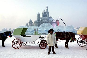 A man stands with his horse and carriage as he waits for visitors in front of a massive ice sculpture