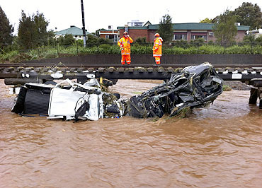 Two state emergency service workers stand on the railway above destroyed vehicles