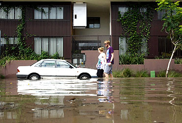 A couple walks past a flooded apartment building in Brisbane