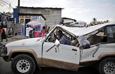 A man smiles as he drives a damage vehicle on a busy street in Port-au-Prince