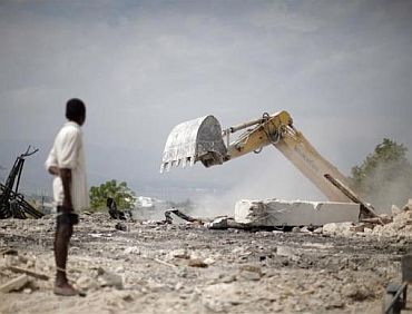 A boy looks at a bulldozer clear rubble from a destroyed church in Port-au-Prince