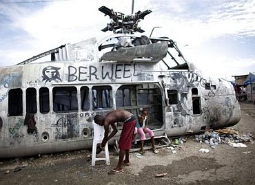 An earthquake survivor washes his hands in a bucket, donated by Haiti's Red Cross to control infections, near a damaged helicopter in a provisional camp in downtown Port-au-Prince