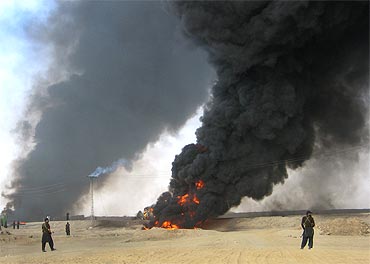 Paramilitary soldiers stand guard as plumes of smoke rise from a burning fuel tanker in Baluchistan