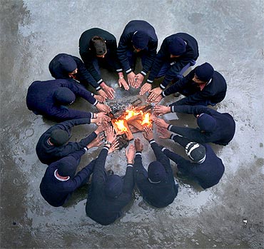 School children sit around a fire to warm themselves during their recess break inside a school in Jammu