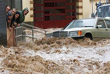 People look on as a street with vehicles is engulfed by heavy flooding in downtown Funchal, Madeira, Portugal, February 20, 2010.