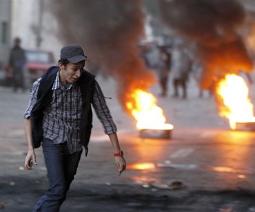 A protester runs in front of burning tyres placed to form a barricade during clashes with riot police in Cairo
