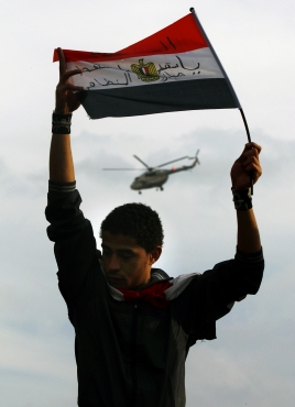 A protester holds an Egyptian flag as an army helicopter flies overhead