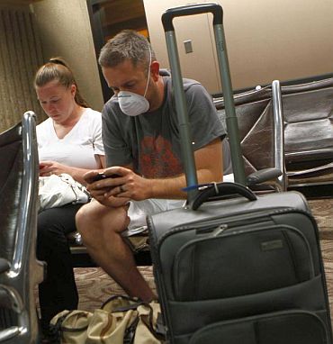 Jason Wallace wears a face mask and plays with his phone as he sits with his wife Emily Wallace inside Sky Harbor International Airport during the storm