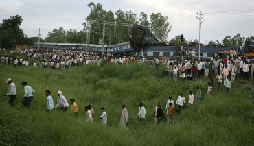 People walk through the grass near the mangled carriages of Kalka Mail which derailed near Fatehpur