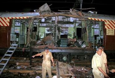 Workers stand near a local train damaged by the serial blasts in Mumbai