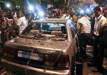 Plainclothed policemen surround a vehicle which was damaged at the site of an explosion in Dadar