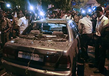 Policemen surround a vehicle which was damaged at the site of an explosion in the Dadar