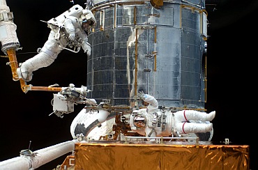 Astronaut Andrew Feustel navigates near the Hubble Space Telescope on the end of the remote manipulator system arm, controlled from inside Atlantis' crew cabin. Mission Specialist John Grunsfeld signals to his crewmate from just a few feet away.
