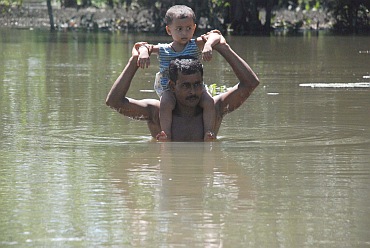 A father wades through water with his son in Lakhimpur