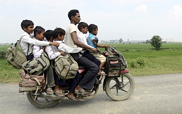 A man rides a motorcycle carrying six children on their way back home from school at Greater Noida