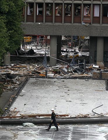 A Norwegian policeman inspects the blast site in front of the destroyed government building in Oslo
