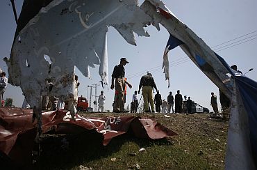 Policemen are seen through a torn billboard as they survey the site of a suicide bomb attack in Swabi on March 30, 2011, that killed 12 persons
