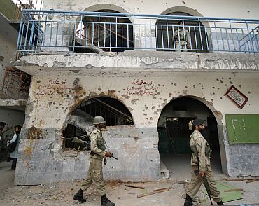 Paramilitary troops walk near a bullet-ridden wall at the Jamia Hafsa, the female Islamic seminary of the Lal Masjid in Islamabad.