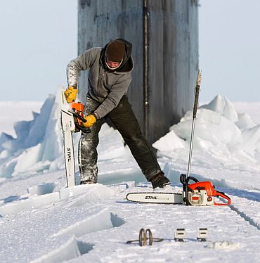 Employee Keith Magness uses a chainsaw to cut through ice to access the hatches of USS Connecticut