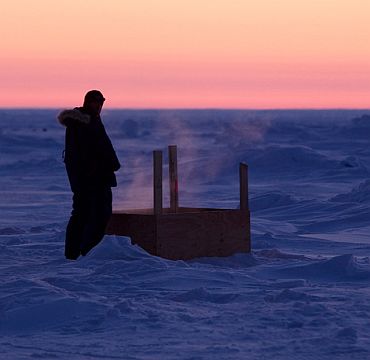 A man urinates into a box as the sun sets over Arctic ice