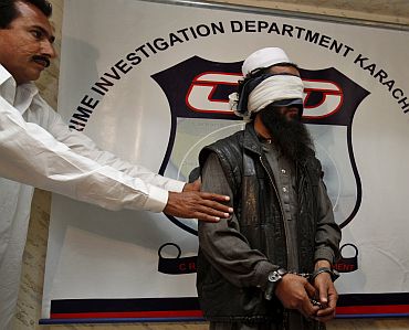 A policeman in plain clothes showcases a blindfolded and handcuffed Mullah Abdul Ghani Baradar in Karachi