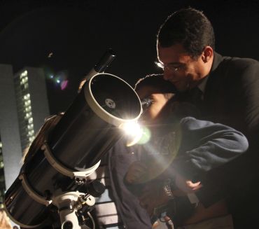 A man helps a boy look through a telescope during a total lunar eclipse