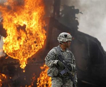 Captain Melvin Cabebe with the US Army's 1-320 Field Artillery Regiment, 101st Airborne Division stands near a burning M-ATV armored vehicle after it struck an improvised explosive device near Combat Outpost Nolen in the Arghandab Valley north of Kandahar