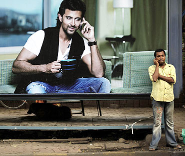 A man makes a phone call on his mobile phone in front of an advertisement for Reliance in Mumbai