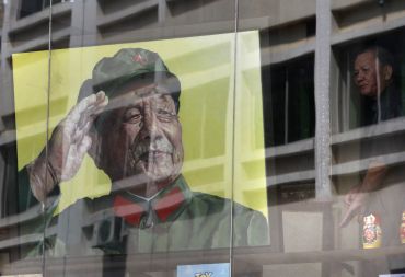 A man looks out from a window next to a portrait of late Chinese leader Deng Xiaoping.