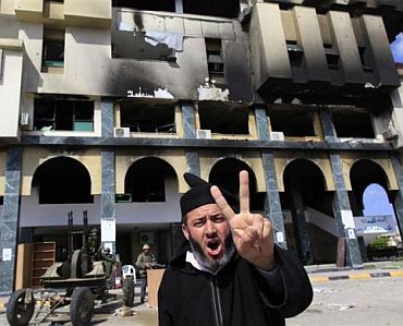 A protester gestures near soldiers opposed to Libya's leader Muammar Gaddafi outside the burnt governor's office in the city of Zawiyah