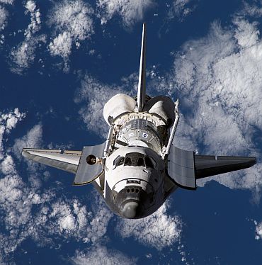 Backdropped by a blue and white Earth, Space Shuttle Discovery approaches the International Space Station during rendezvous and docking operations