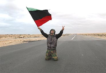 An anti-Gaddafi rebel prays and chants along a road